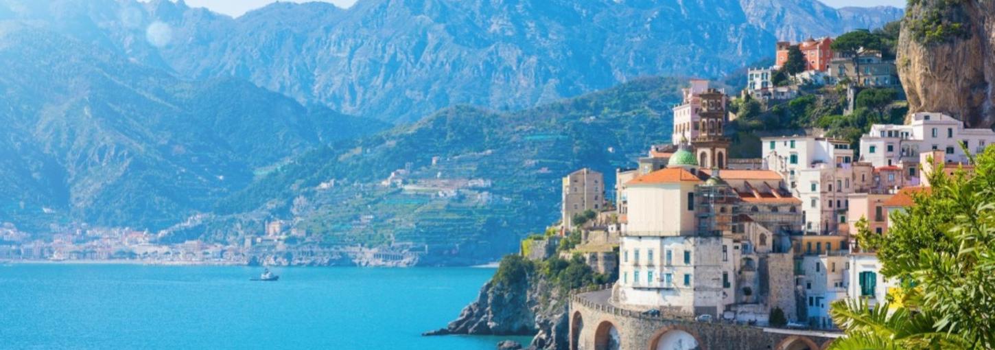 A view of the Amalfi Coast with a village and rolling mountains surrounding the water.