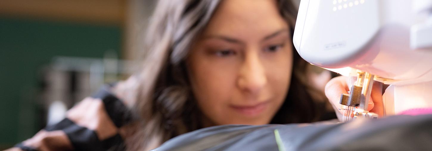 Close-up of a sewing machine with a woman in the background.