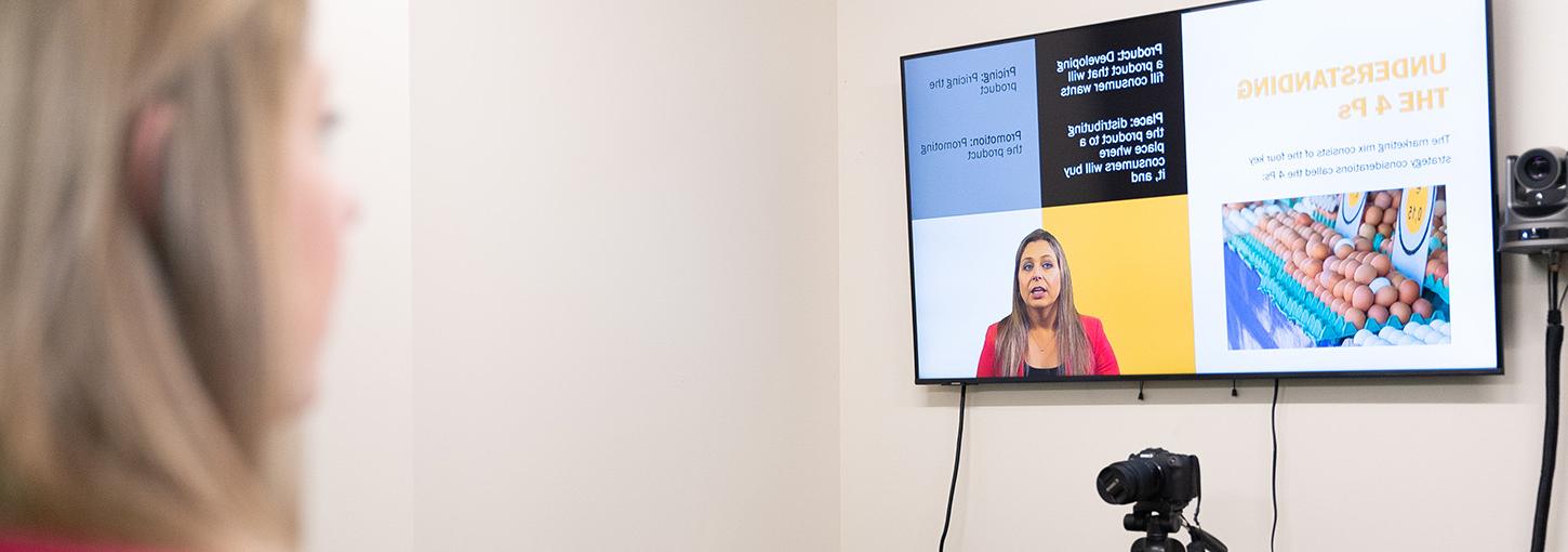 Professor Mya Groza watches herself on a monitor next to cartons of eggs as a video camera records her lecturing.